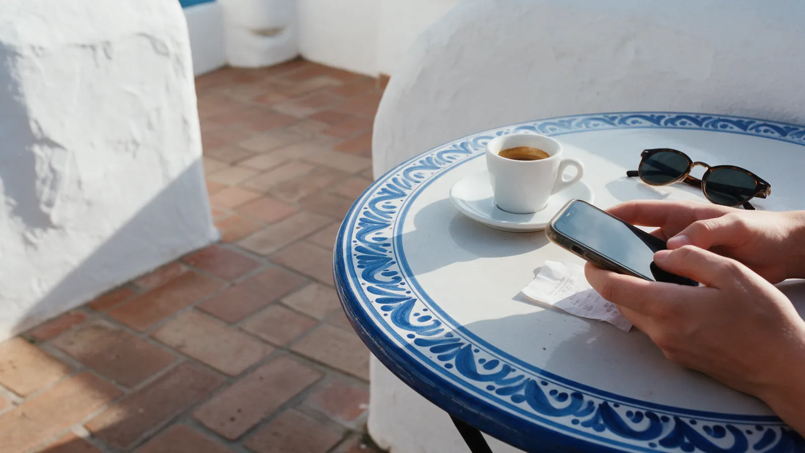 A hand photographs a café receipt with a phone on a blue and white tiled table.